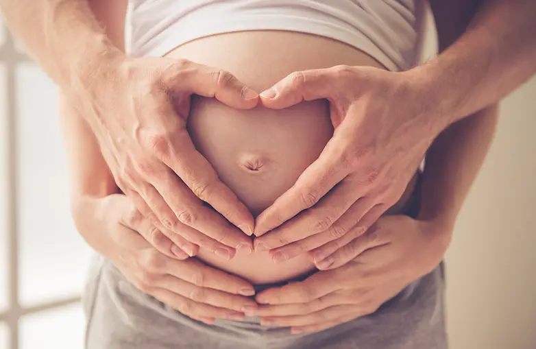 Closeup photo of hands making a heart sign over the belly of pregnant woman
